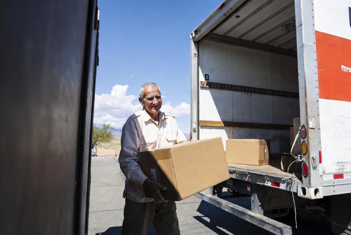 Active senior man carrying a moving box with desert mountains in the background, representing independent living in the Coachella Valley